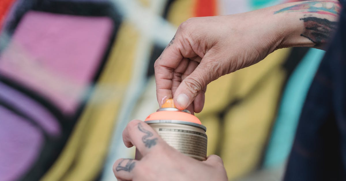 What is the proper way to maintain a can opener? - Soft focus of crop unrecognizable painter with tattoos opening spray paint can while standing near colorful wall with creative graffiti