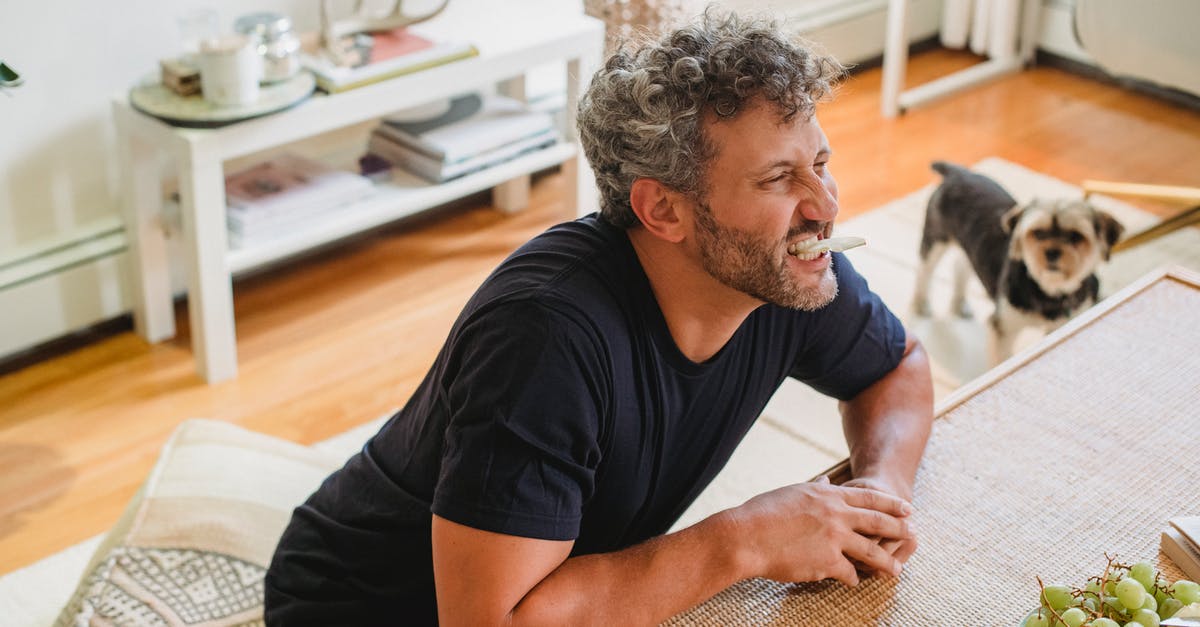 What is the proper way to make a fruit purée? - Cheerful adult male with beard and grey curly hair making faces with piece of apple in teeth