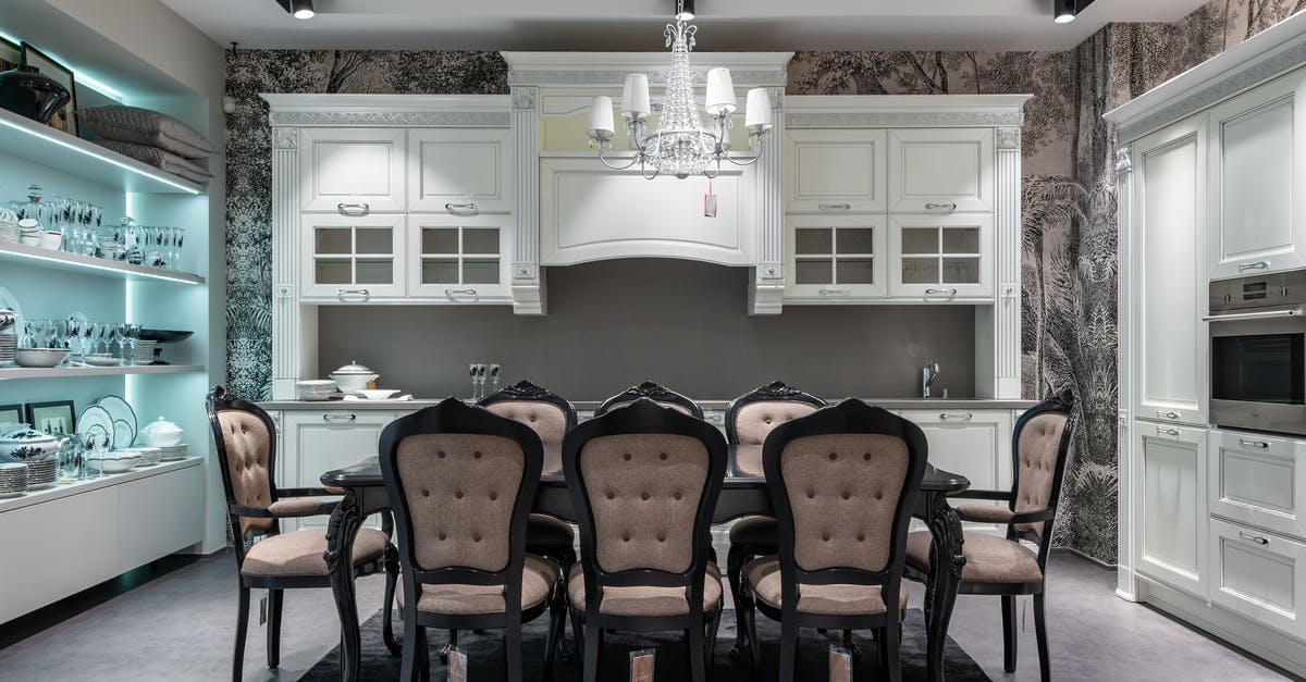 What is the purpose of the storage beneath an oven? - Chairs at table placed in spacious kitchen with oven near white cabinets and storage cupboard with various tableware in apartment