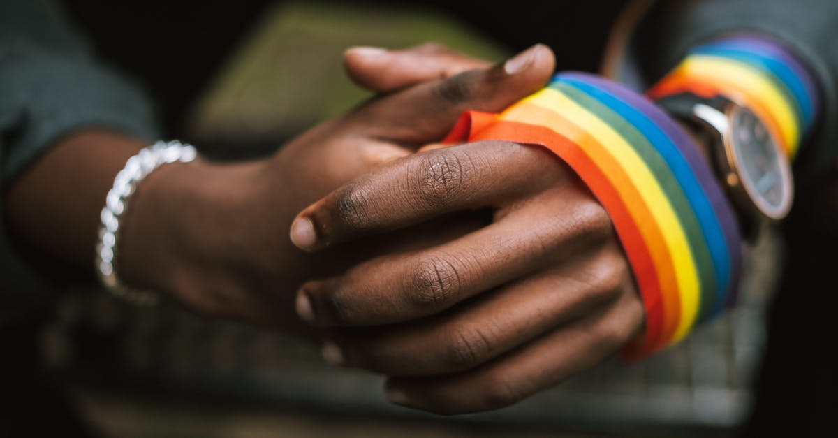 What is the right consistency for ghee? - Crop anonymous African American homosexual male wearing colorful rainbow ribbon on arm while sitting on street with hands clasped