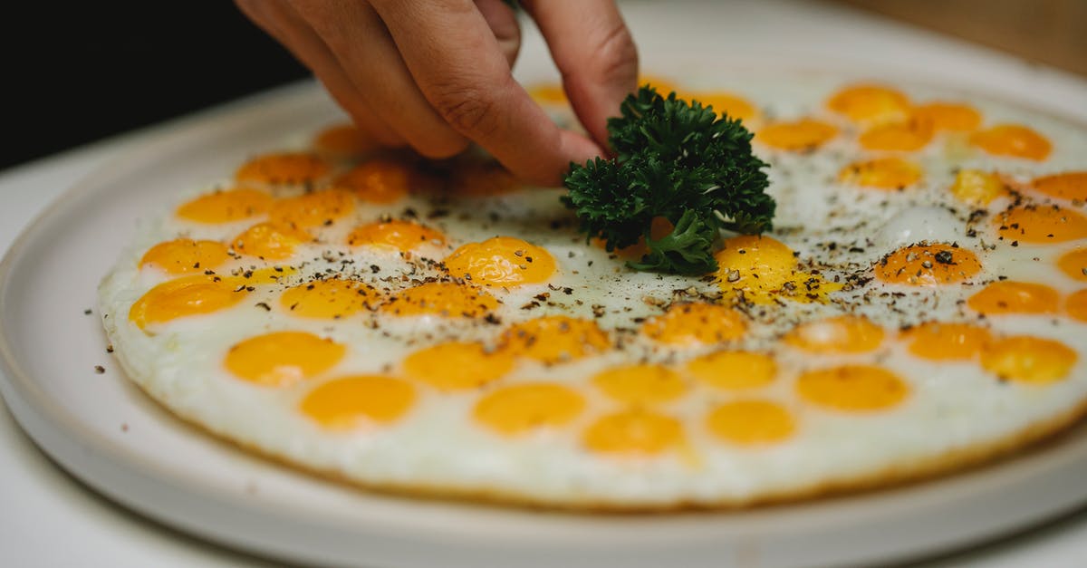 What is the term for serving a soft-cooked fried egg that breaks when the meal is consumed? - Crop unrecognizable chef garnishing fried eggs with herbs