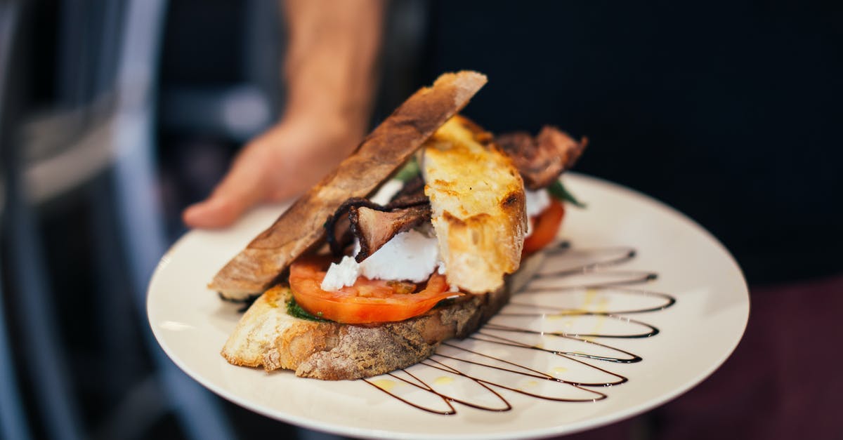 What is the term for serving a soft-cooked fried egg that breaks when the meal is consumed? - From above of crop unrecognizable waiter holding plate of appetizing sandwich with bacon tomatoes and poached eggs in crispy toasted bread