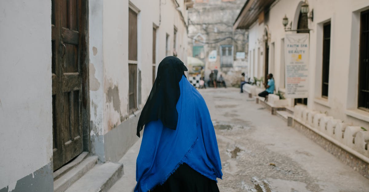 What is the traditional way to layer a lasagna? - Back view of anonymous Muslim female wearing traditional hijab and cloak walking along narrow street in old city