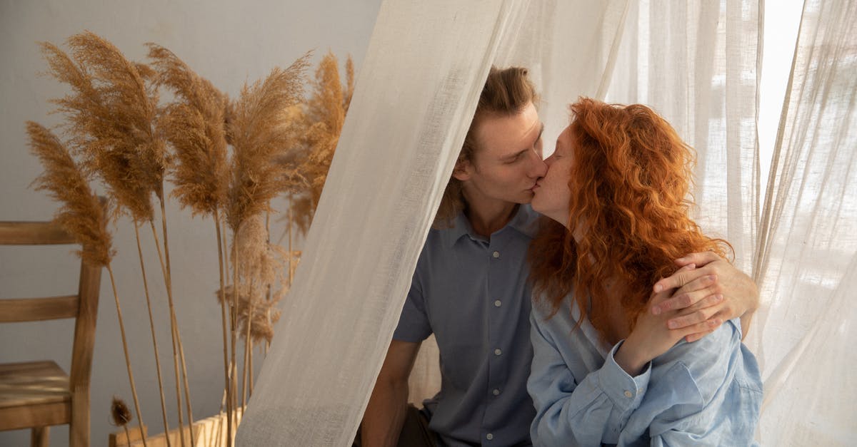 What is the white sediment / residue found in ginger juice? - Redhead girlfriend and boyfriend kissing and holding hands while sitting near window with white curtain in room with dry plants