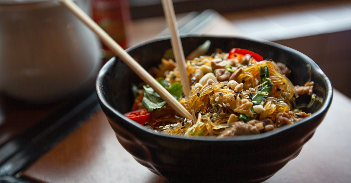 What is this Asian dish made with boiled vegetables?  - Delicious appetizing Asian noodles with vegetables and nuts served in bowl with chopsticks on table