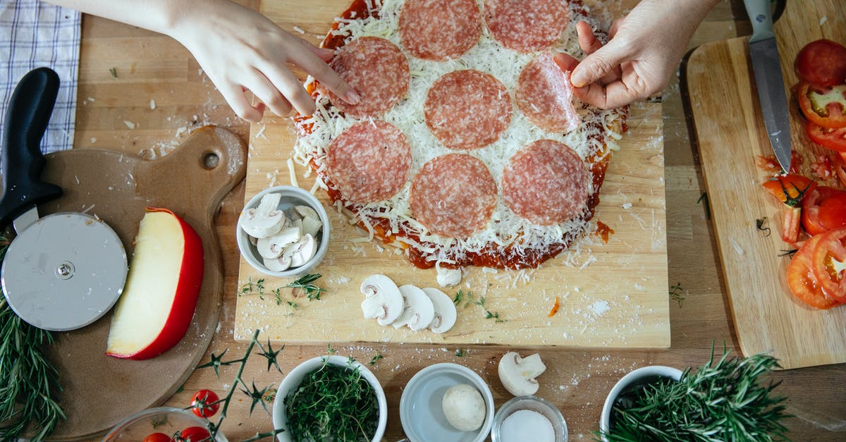 What is this French cuisine technique called, where "a piece of pheasant meat is cooked between two slices of veal, which are then discarded?" - Top view of crop unrecognizable people adding salami in homemade pizza placed on wooden table among various fresh ingredients while cooking together