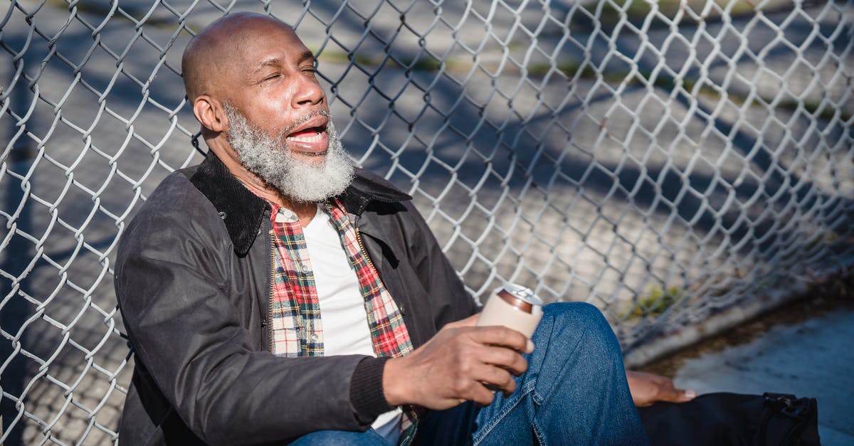 What is this grilling utensil with two wire mesh panels? - African American senior man with closed eyes and opened mouth sitting near metal fence and holding beer can