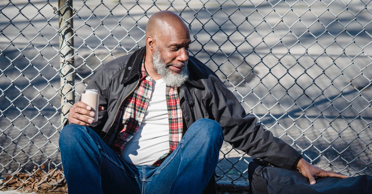 What is this grilling utensil with two wire mesh panels? - Hairless aged ethnic male in casual outfit touching bag while sitting against mesh fence with beer can