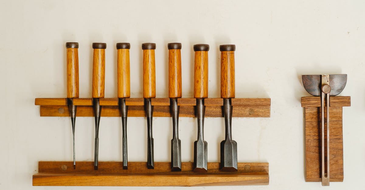 What is this metal utensil tool with wooden handle? - Collection of metal chisels with wooden handles and wood cutters for woodwork arranged on shelf on white wall in workshop