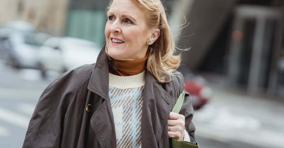 What kind of nonstick coating is this? - Cheerful senior female in coat with bag and flying hair looking away on urban road in daytime