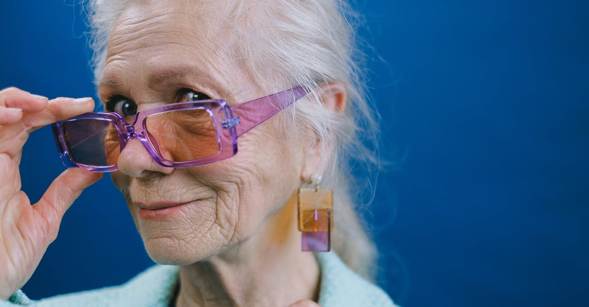 What kind of pickle was this? - Portrait of elegant smiling gray haired elderly female wearing purple sunglasses and earrings looking at camera against blue background