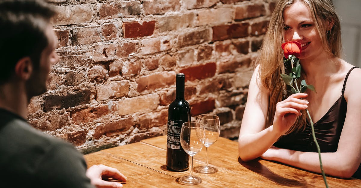 What made these red lentils 'brick' together? - Young couple in elegant clothes sitting at wooden table near brick wall in light restaurant while enjoying date with red rose and wine near glasses and looking at each other