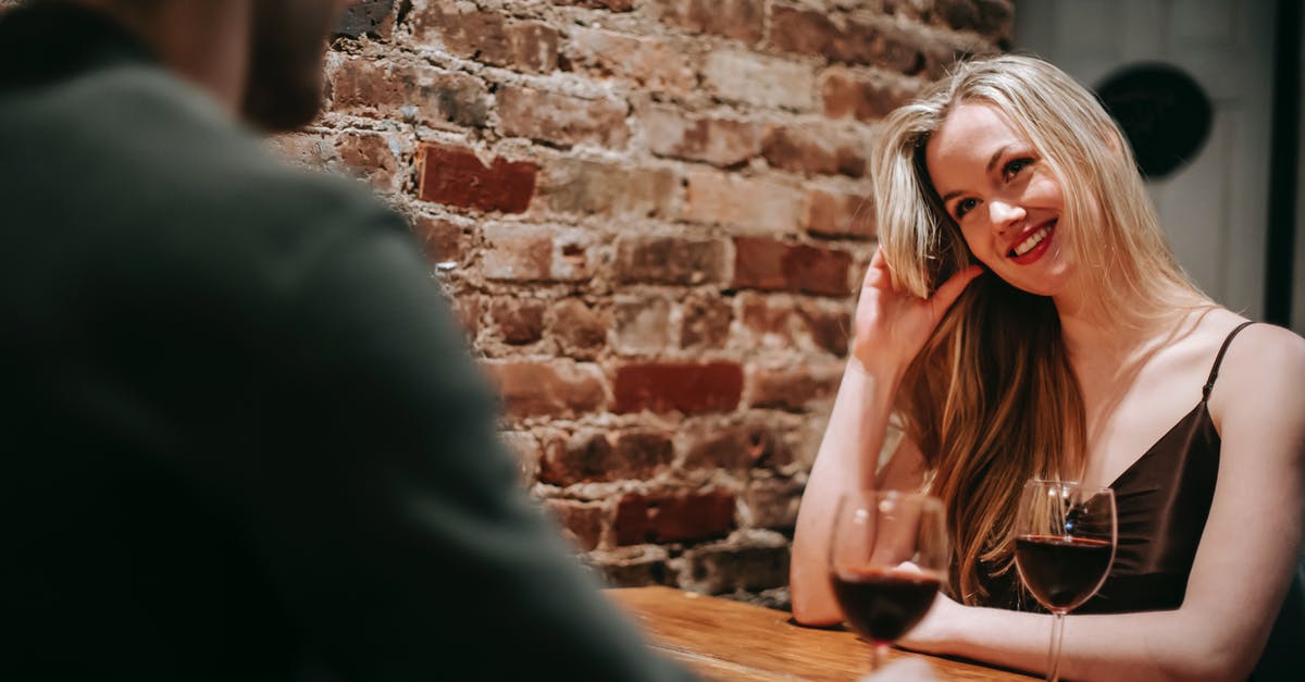 What made these red lentils 'brick' together? - Young couple in elegant outfits sitting in light cafeteria at wooden table near brick wall and having romantic dinner with red wine in glasses and looking at each other happily