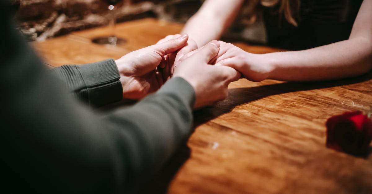 What made these red lentils 'brick' together? - Crop anonymous couple sitting in light cafeteria at wooden table with glass with wine and red rose near brick wall and having romantic dinner while holding hands gently