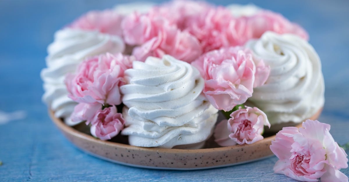 What makes a souffle rise? - From above of delicious white marshmallows zephyr and buds of pink flowers placed on plate on blue table in room against blurred background