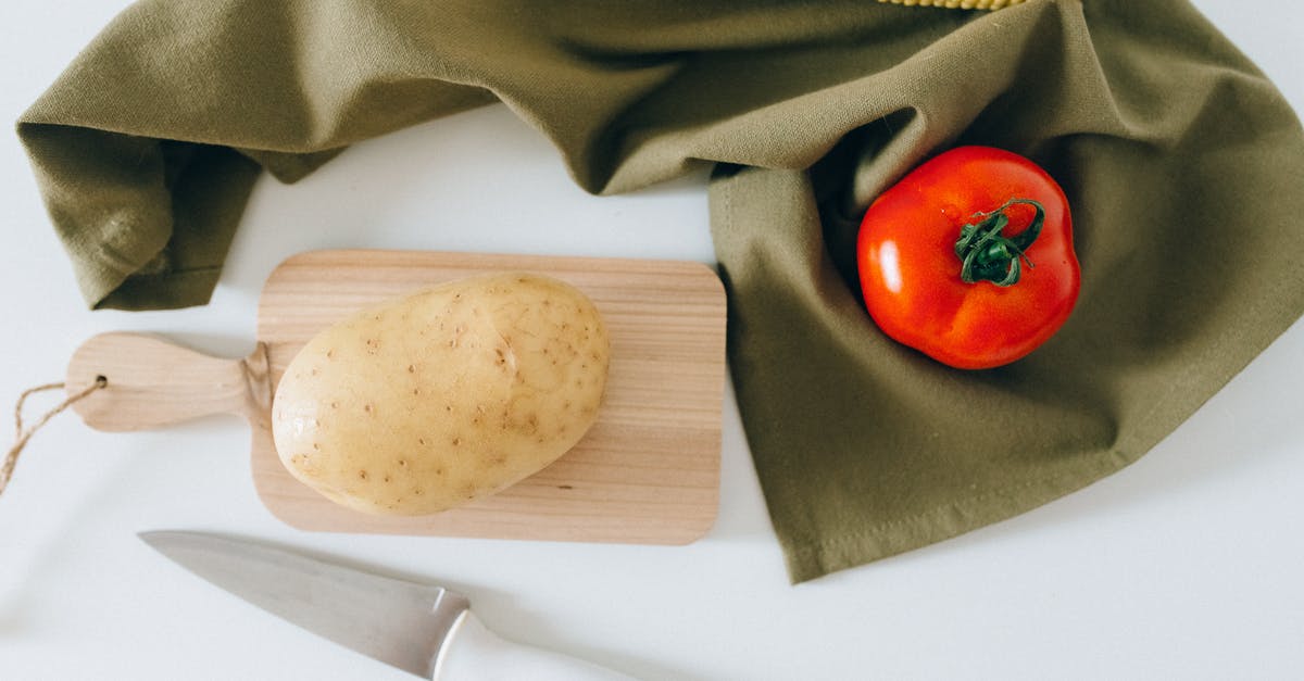 What methods make tomato chopping less messy? - A Potato on a Wooden Chopping Board Beside a Tomato and Corn