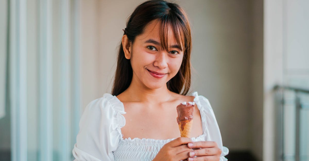 What non-dairy filler to use in white chocolate style coatings? - Cheerful Asian female in white outfit with sweet chocolate ice cream cone in hand looking at camera while standing on balcony