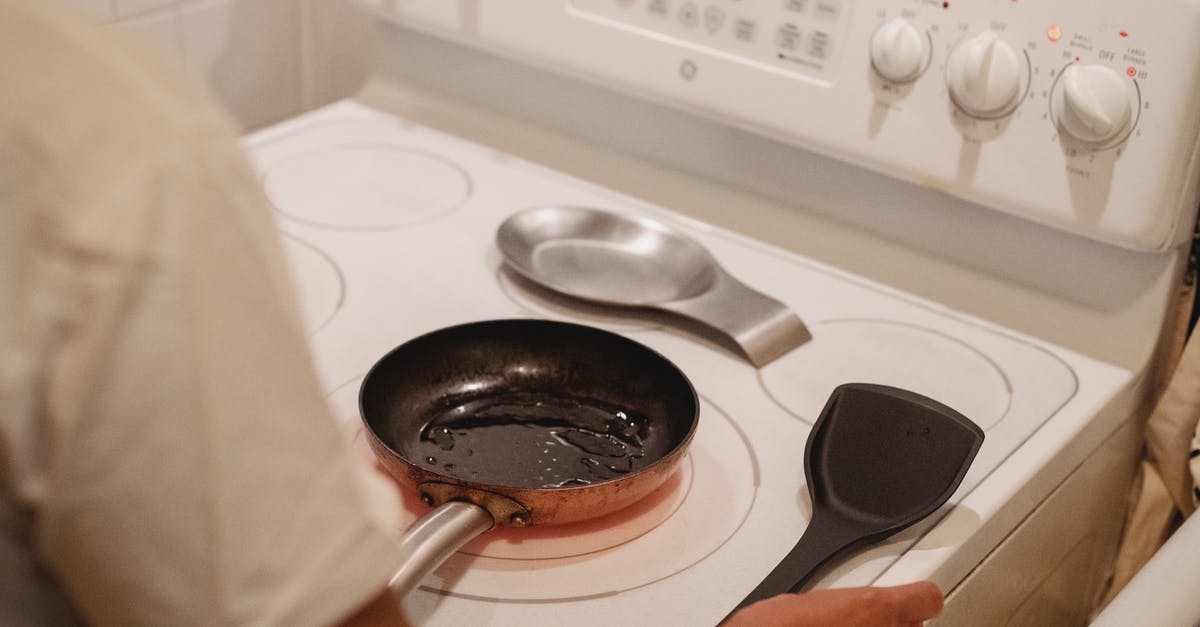 What oil is best for seasoning a cast-iron skillet - Crop unrecognizable person near white stove with black spatula cooking scrambled eggs in kitchen