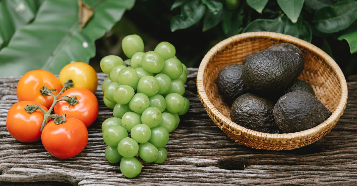 What pickled yellow-green vegetable is this, in Chiu Chow Garden's appetizer? - High angle composition of ripe fresh tomatoes green grapes and avocados in wooden bowl placed on bench in lush garden during harvest season