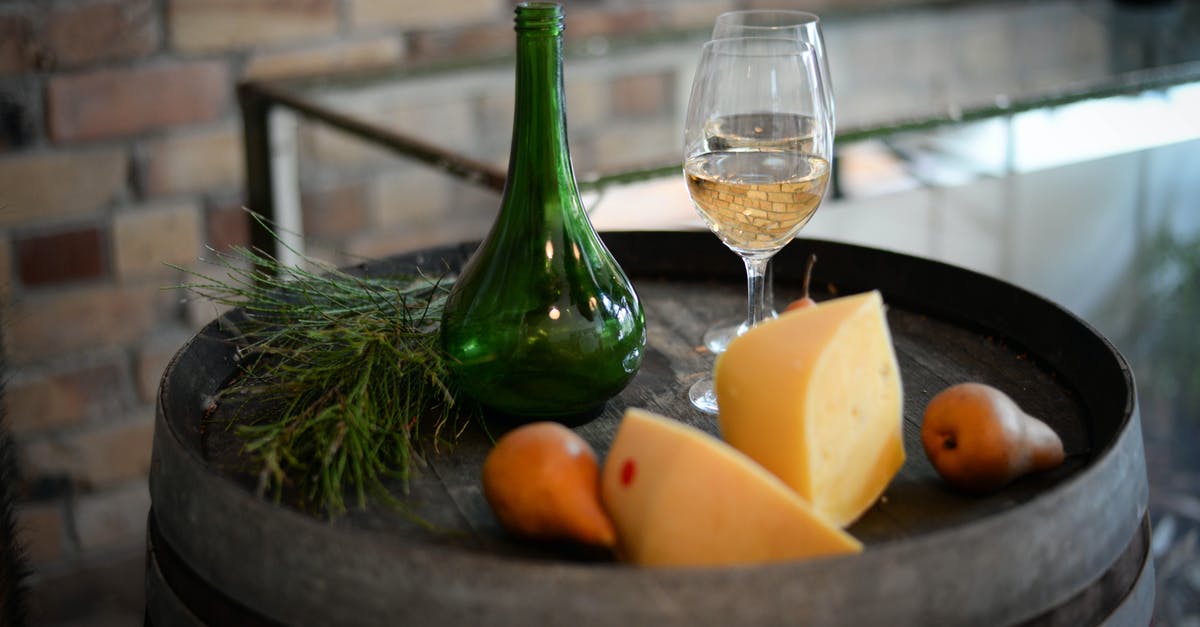 What role does alcoholic liquid play in cheese fondue recipes? - High angle of glass bottle with wineglasses placed on barrel with aromatic cheese and pears