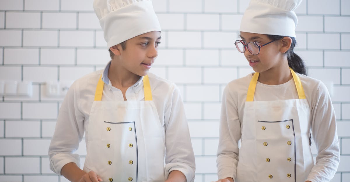 What should I look for in a good, multi-purpose chef's knife? - Kids in White Apron and Chef's Hat Looking at each Other while Standing Near the Countertop