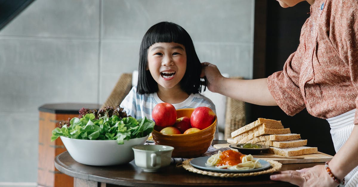 What should I look for when buying a pasta roller? - Crop unrecognizable female in apron standing near table and caressing child while having breakfast together at home