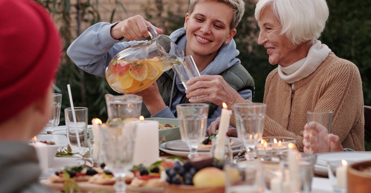 What side dish should I have with saltimbocca? - Positive lady pouring drink into glass for elderly woman while having dinner with family on terrace