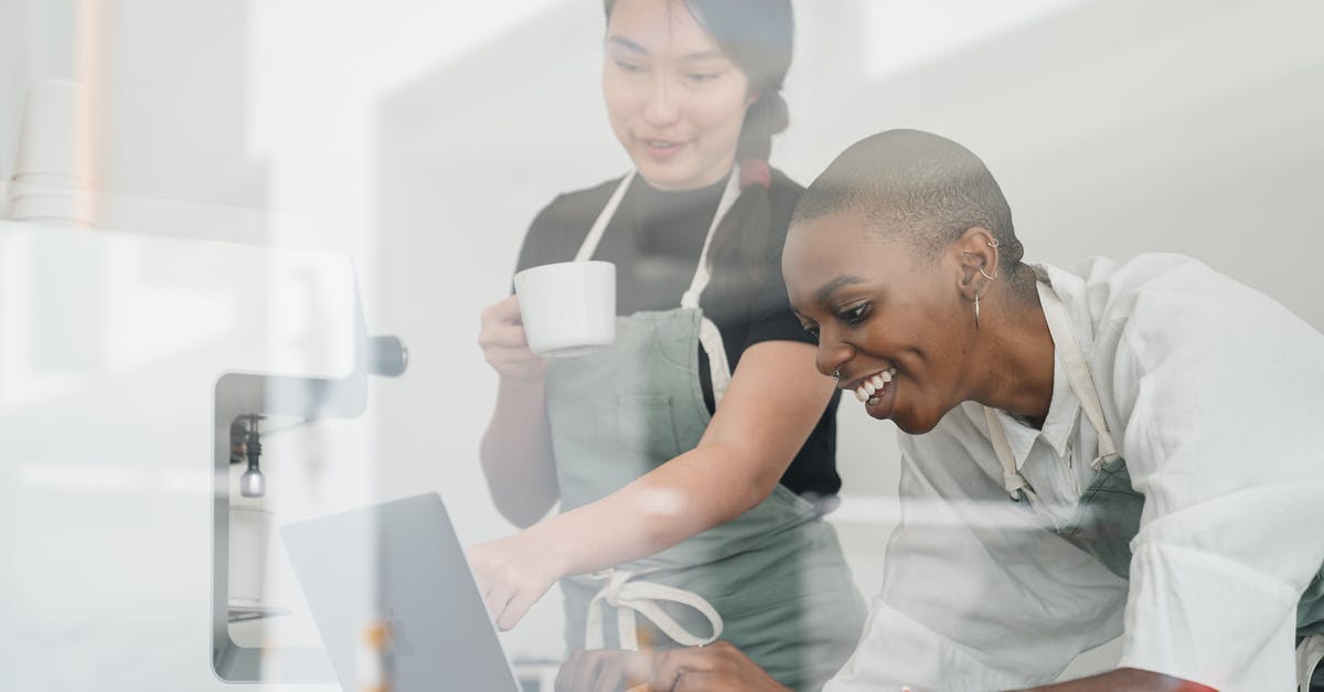 What special knowledge or skills about coffee do baristas have? - Through glass of friendly young Asian head barista showing young cheerful African American female coworker how to use special program on laptop