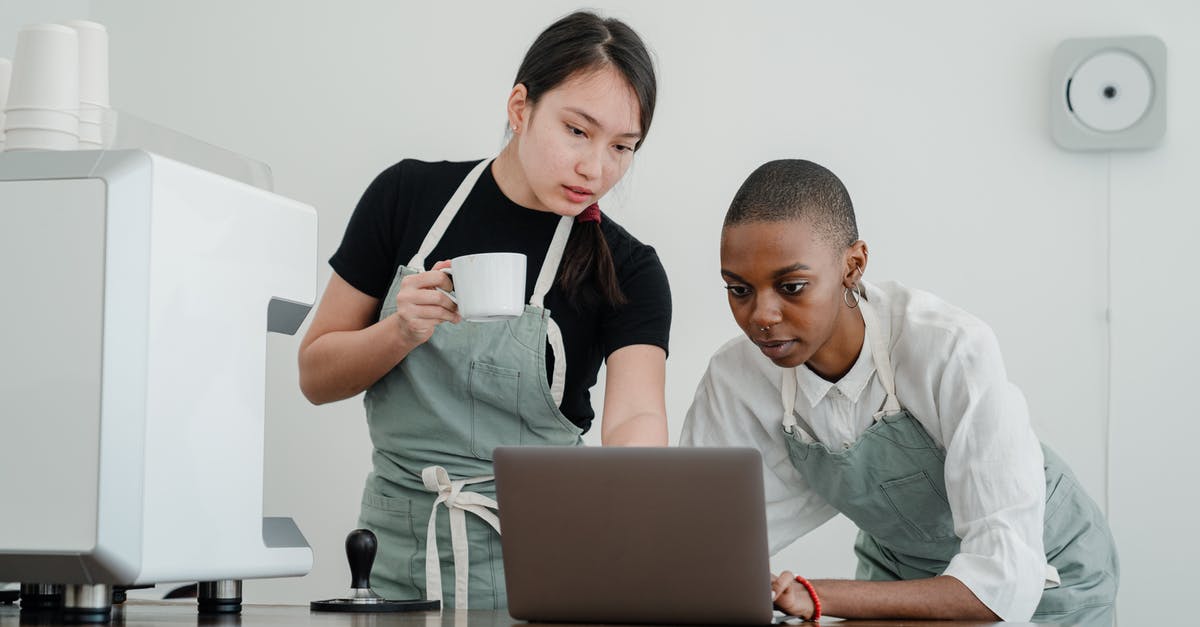 What special knowledge or skills about coffee do baristas have? - Serious Asian female barista with coffee in hand teaching new black colleague to use computer program while standing at table with laptop