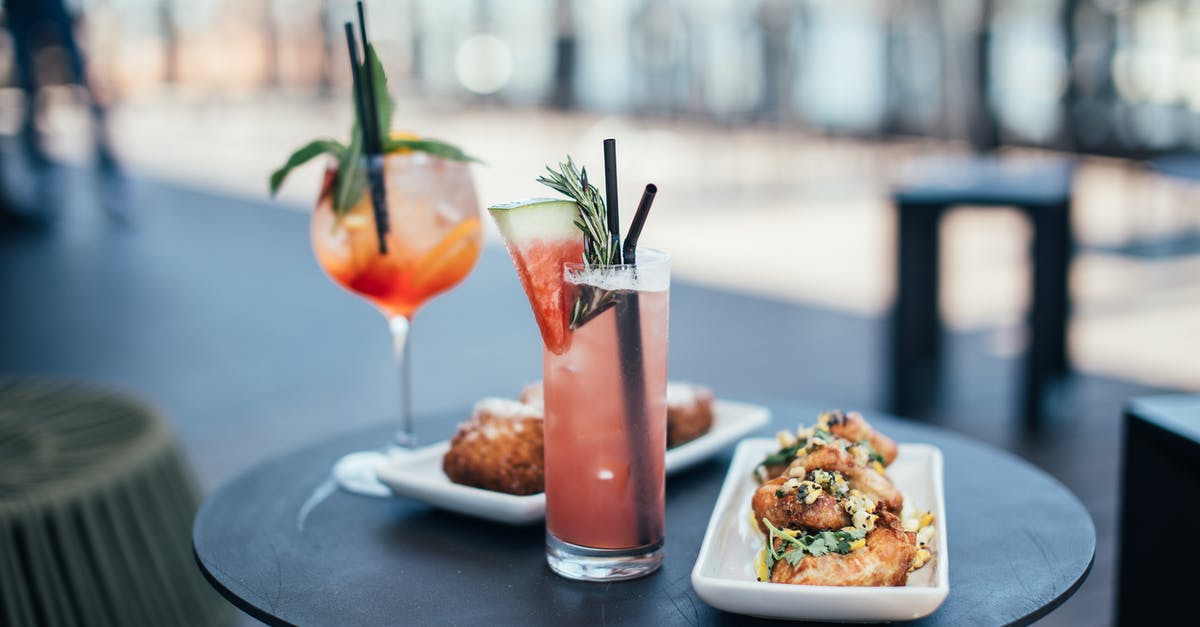 What species of red round watermelon is this? - Glasses with colorful cocktails garnished with green herbs and straws with watermelon slice near white plates with delicious appetizers on round table in street restaurant in daytime