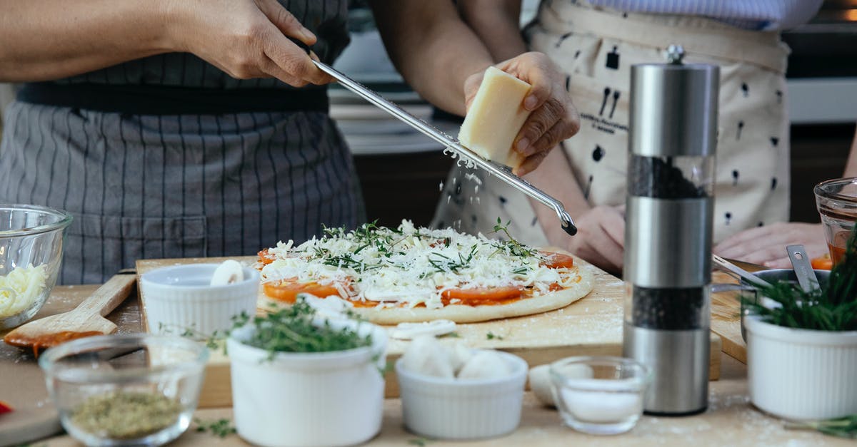 What spice rub would be typically Thai? - Unrecognizable female cooks grating cheese on homemade pizza at table with various ingredients and condiments in kitchen during cooking process