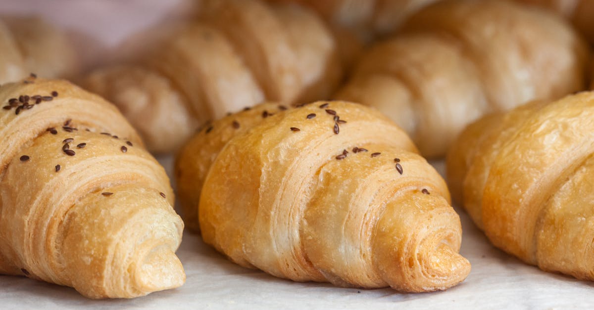 What techniques or tricks make soft, flaky pastries instead of leathery ones? - Delicious baked croissants with little brown sesame seeds on top placed on white cloth in bakery