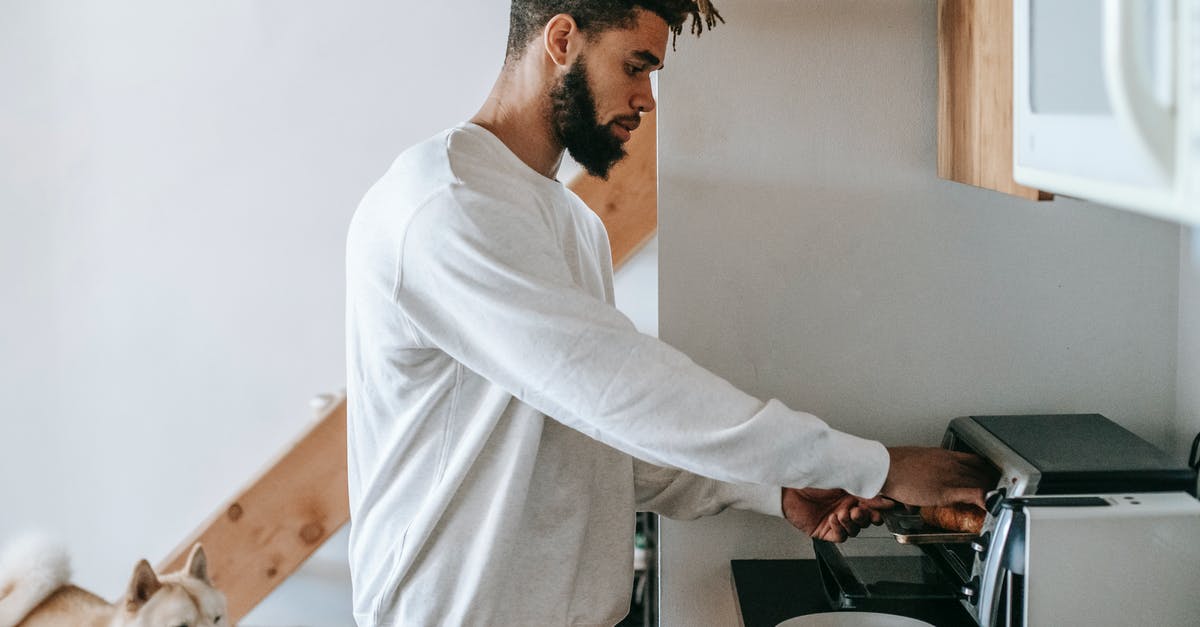 What to do to cool down oven after grease fire? - Bearded young black man heating croissant in microwave oven standing near dog