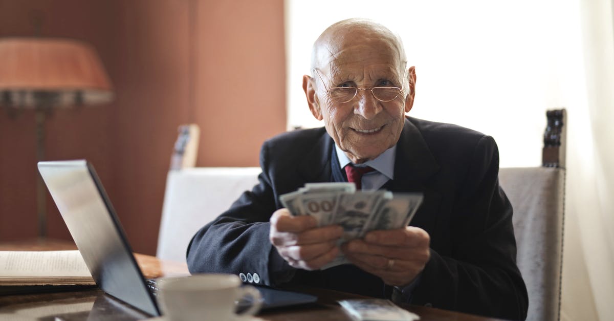 What to do with old coffee beans? - Confident senior businessman holding money in hands while sitting at table near laptop