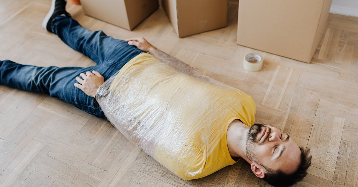 What to use instead of cling film to wrap pastry - High angle of tired male in casual wear wrapped in plastic tape and lying on parquet with eyes closed near carton boxes during relocation