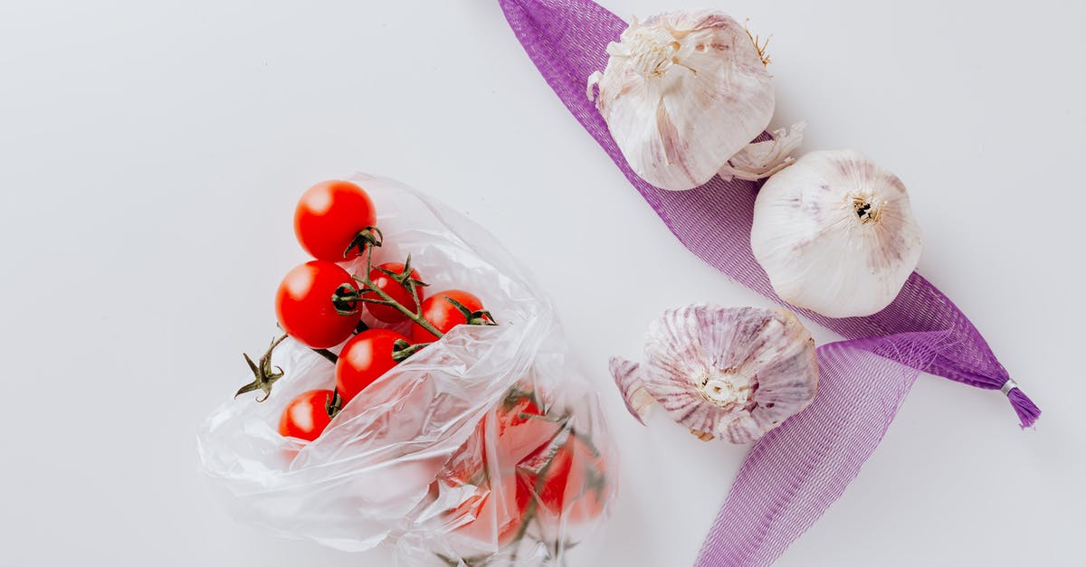 What turned my garlic purple? - Top view of fresh cherry tomatoes in transparent polyethylene bag and three heads of garlic placed on purple grid isolated on white background