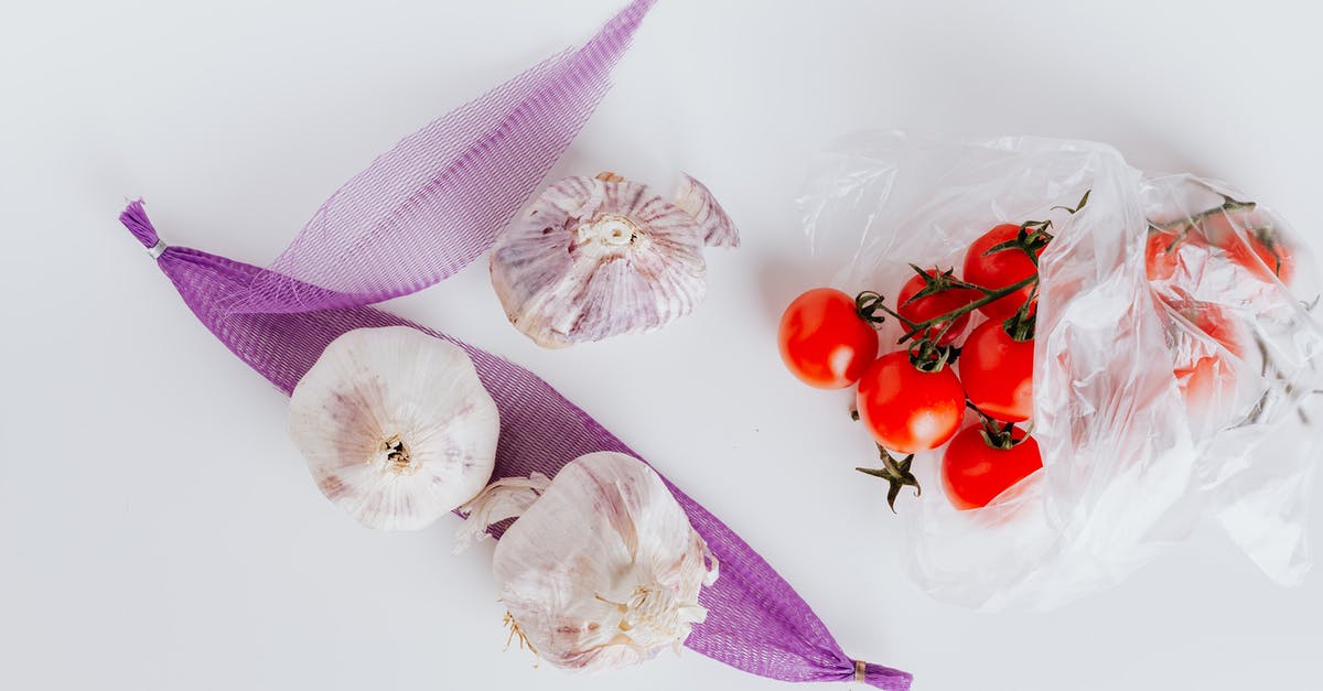 What turned my garlic purple? - From above of bunch of ripe tomatoes put in plastic bag near raw heads of garlic put on violet transparent net on white surface