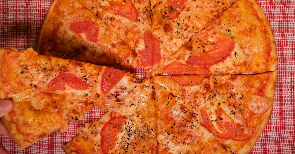 What type of cheese is used on Patsy's Old Fashioned Margherita Pizza - Top view of crop anonymous person taking slice of yummy pizza with tomato and oregano placed on checkered tablecloth