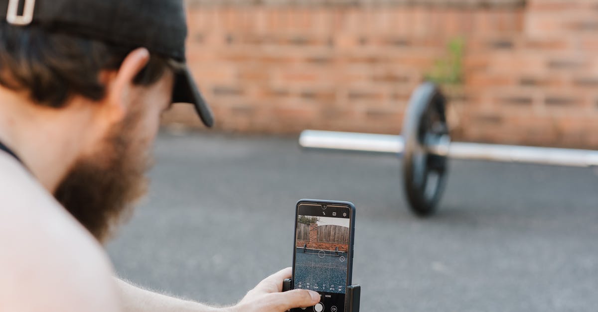 What type of whetstones are you using for sharpening stainless steel knives? - Crop anonymous unshaven sportsman in cap taking photo of barbell on cellphone on pavement in town