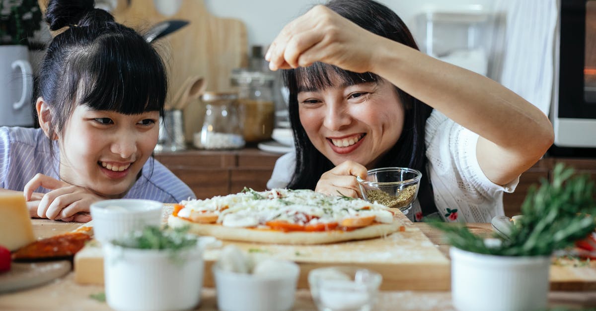 When do you add spices to homemade butter? - Happy women adding spices on pizza