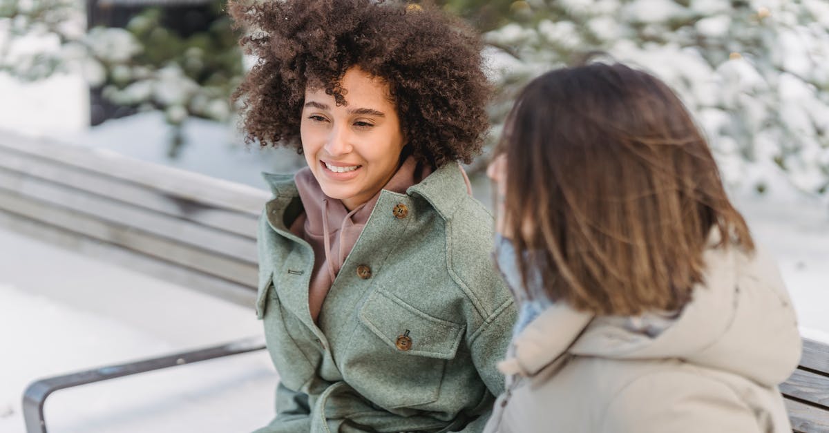 When is the best time to freeze bread? - High angle of positive African American female with curly hair sitting on bench near girlfriend while spending time in winter park