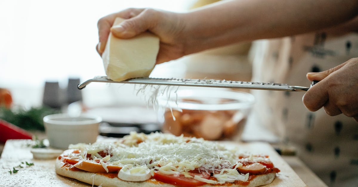 When should I add spinach to homemade pizza? - Side view of crop unrecognizable person grating piece of hard cheese on palatable homemade pizza in kitchen at daytime