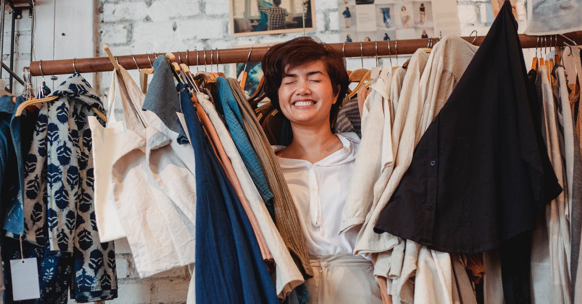 Where can I buy Prime Beef? [closed] - Cheerful Asian female customer standing among hanging clothes in store and smiling