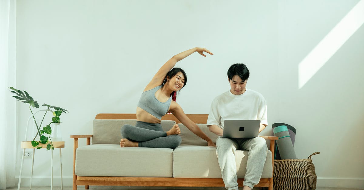 Which cooking device allows flexible temperature programming? - Full body of Asian male using laptop while happy female stretching body on sofa in light living room