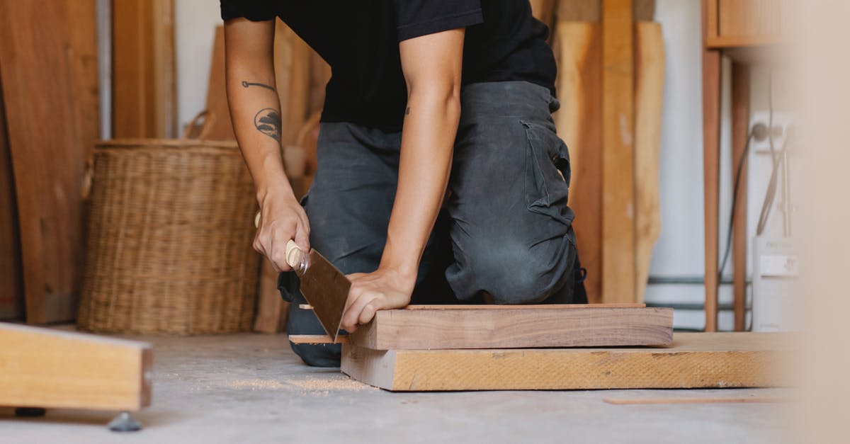 Which cut makes cheapest goulash? - Crop anonymous male with tattoo sawing piece of timber detail with planer in workshop