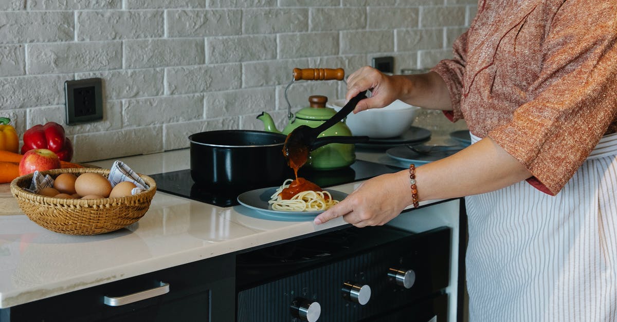 Which is a typically American way of seasoning spaghetti and other pasta? - Side view crop housewife in apron cooking lunch in kitchen and adding fresh delicious tomato sauce to Italian pasta