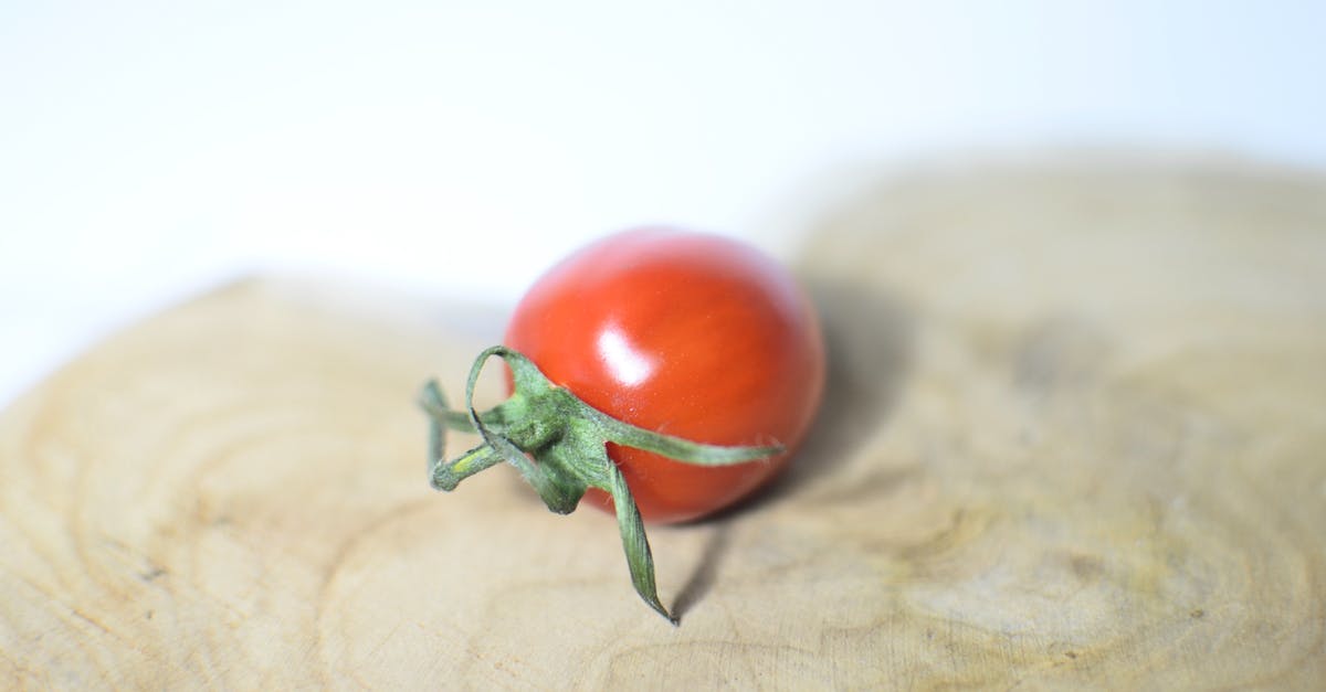 Which is the most caloric, edible, single ingredient by weight? - Closeup single small ripe cherry tomato placed on shaped wooden cutting board on white table on blurred background in light kitchen