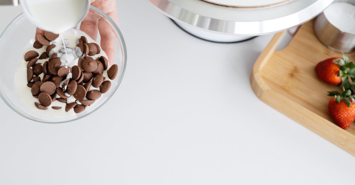 Whipping heavy cream with melted chocolate - From above of crop unrecognizable female adding hot ganache made of heavy cream to dark chocolate drops in glass bowl