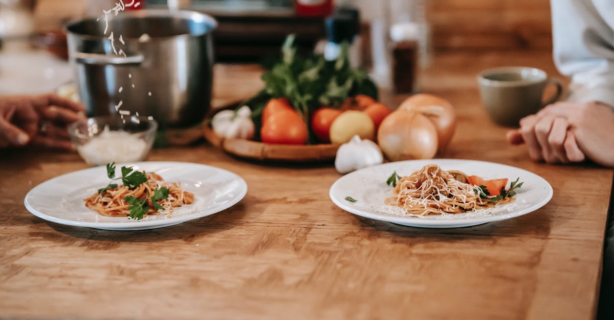 Why add pasta water to pasta sauce? - High angle of crop anonymous woman sitting at table near husband adding grated cheese on appetizing homemade spaghetti