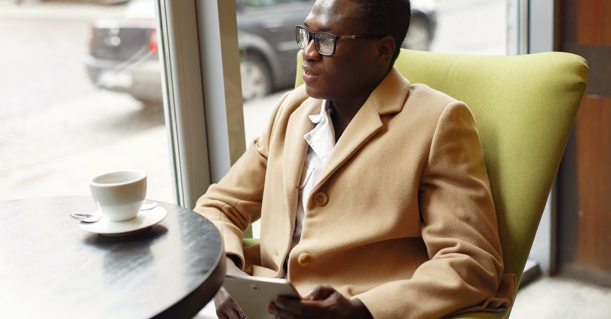 Why boil and cool jam before using it in a cake? - Serious African American male in trendy formal suit and eyeglasses sitting on cozy chair in cafe with cup of coffee and browsing tablet